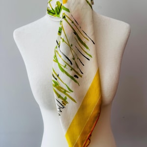 May include: A square scarf featuring an off-white base with a printed pattern of green and black abstract grass-like lines. The scarf includes a prominent solid yellow border along one side and is tied around a white mannequin neck form.