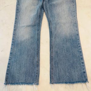 Puede incluir: Vaqueros de mezclilla azul claro con pernera acampanada y dobladillo deshilachado. Los vaqueros tienen un dise&ntilde;o cl&aacute;sico de cinco bolsillos y un lavado descolorido. La mezclilla es de peso medio y tiene un aspecto ligeramente desgastado.