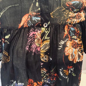 May include: Black button-down shirt with a floral pattern in shades of orange, pink, and blue. The shirt has a mandarin collar and short sleeves. The fabric appears to be lightweight and semi-sheer.