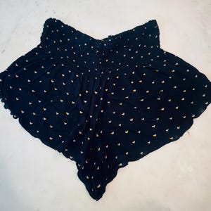 May include: Navy blue shorts with a high, elasticized waist and a scalloped hem. The shorts are covered in tiny white and yellow heart-shaped patterns. The fabric appears to be lightweight and flowy.
