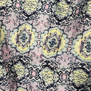 K&ouml;nnte beinhalten: Nahaufnahme eines Stoffes mit einem sich wiederholenden geometrischen Muster. Das Design weist eine Mischung aus Farben auf, darunter Marineblau, Hellgelb, Hellrosa und Grau. Das Muster hat ein symmetrisches, fast florales Aussehen mit komplizierten Details.