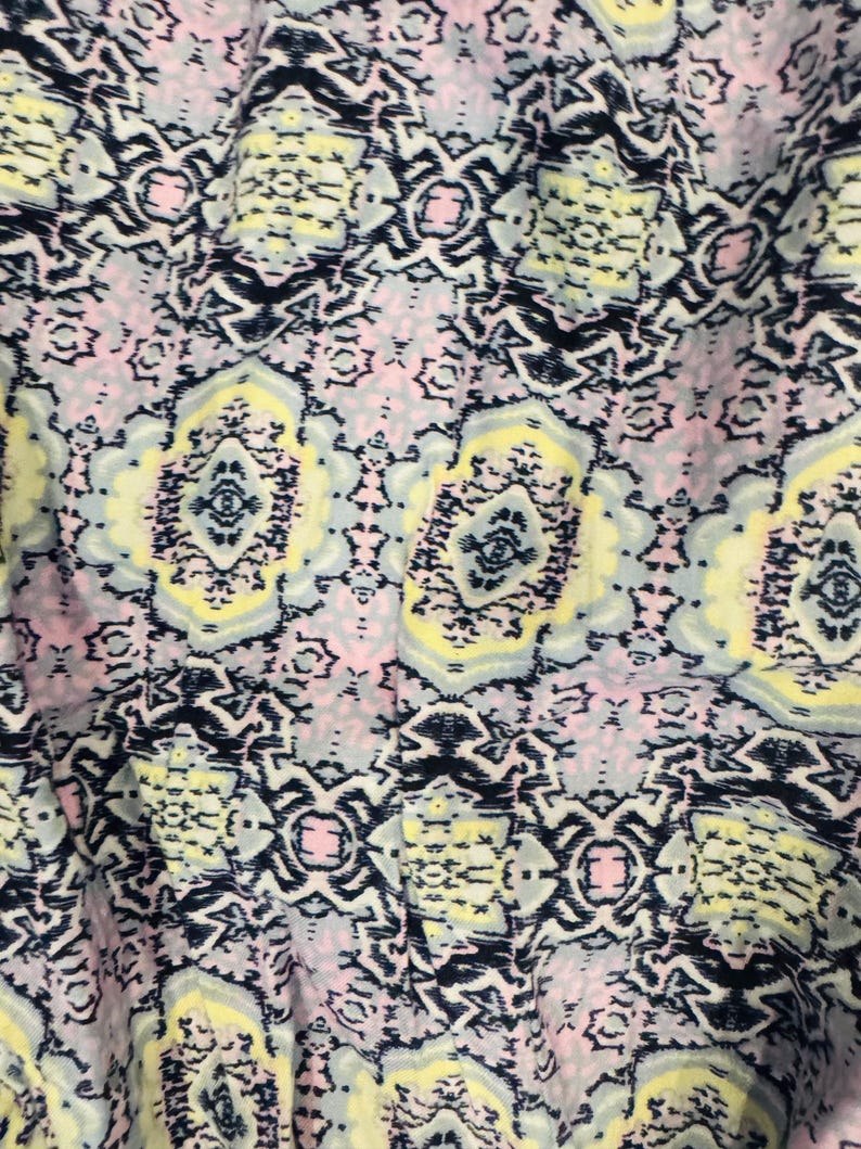 K&ouml;nnte beinhalten: Nahaufnahme eines Stoffes mit einem sich wiederholenden geometrischen Muster. Das Design weist eine Mischung aus Farben auf, darunter Marineblau, Hellgelb, Hellrosa und Grau. Das Muster hat ein symmetrisches, fast florales Aussehen mit komplizierten Details.