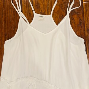 Puede incluir: Un camis&oacute;n blanco con tirantes finos y cuello en V. La parte superior tiene un dise&ntilde;o fluido con un dobladillo con volantes. La etiqueta dice "INTIMATELY". La prenda est&aacute; hecha de una tela ligera.