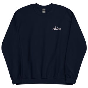May include: Navy blue sweatshirt with the word "chica" embroidered in a cursive font on the upper chest. The sweatshirt has a crew neck and long sleeves. The Gildan brand label is visible at the back of the neck.