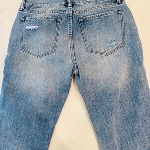 Puede incluir: Vaqueros de mezclilla azul claro con detalles desgastados, incluyendo roturas en los bolsillos traseros. Los vaqueros tienen un dise&ntilde;o cl&aacute;sico de cinco bolsillos y un lavado descolorido.