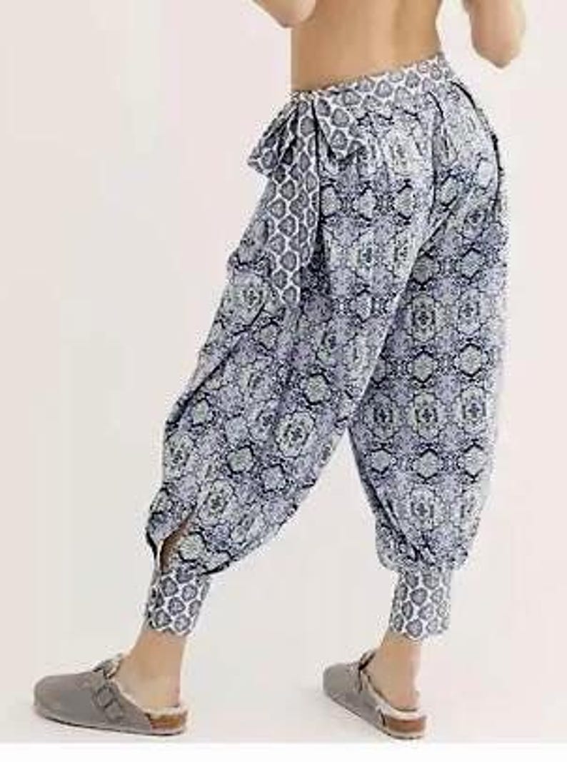 K&ouml;nnte beinhalten: Haremshose mit blau-wei&szlig;em Muster, geraffter Taille und Kn&ouml;chelb&uuml;ndchen. Die Hose hat eine lockere Passform und eine dekorative Schleife. Der Stoff weist ein sich wiederholendes geometrisches Design auf. Die Hose ist ca. 100 cm lang.