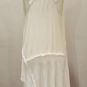 Puede incluir: Vestido blanco sin mangas con tirantes finos y dobladillo asim&eacute;trico. El vestido presenta un dise&ntilde;o en capas con bordes sin rematar, lo que le da una est&eacute;tica bohemia o vintage. El vestido se exhibe en un maniqu&iacute;.