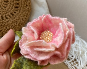 May include: A pink felt flower with a centre of pearl beads. The flower has green felt leaves.