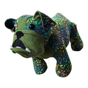 May include: A handmade plush bulldog in shades of green. The bulldog's head and ears are a solid green, while the body features a colorful, speckled pattern. It has black button eyes, a black nose, and white felt teeth.