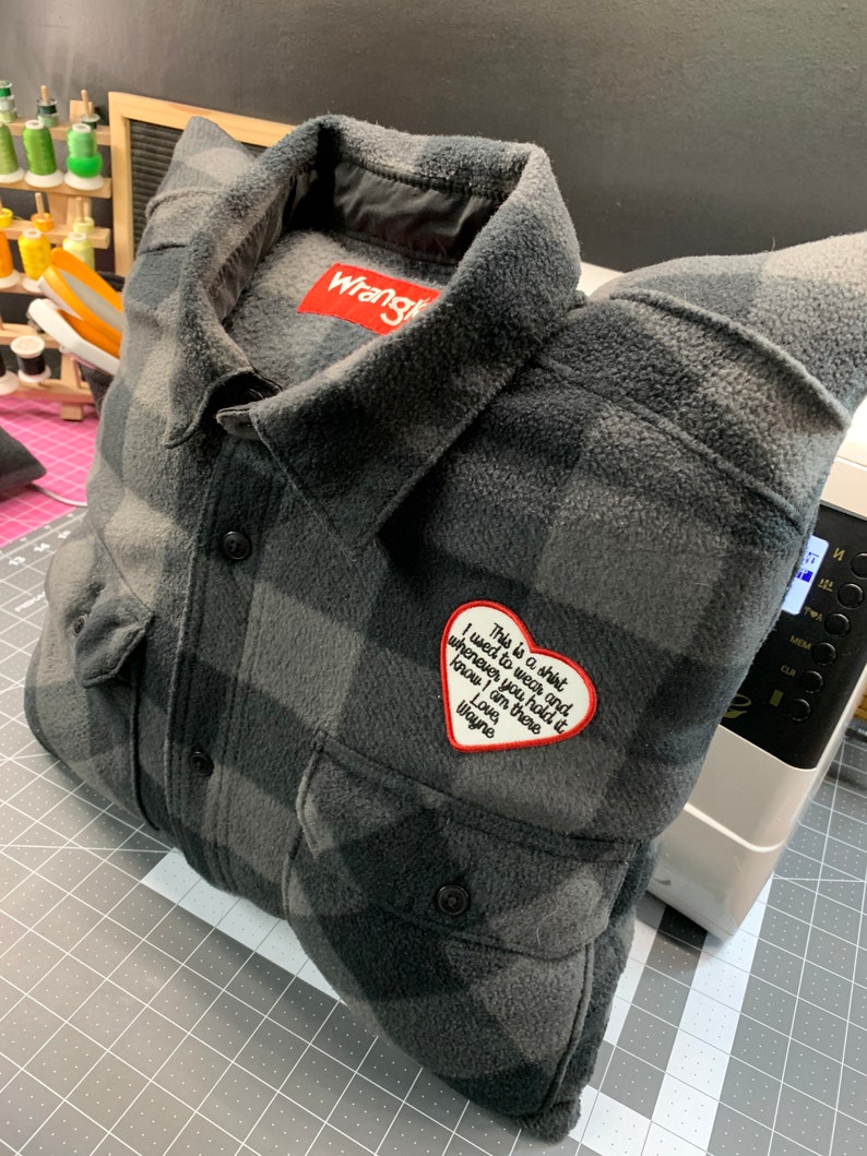 May include: A gray and black plaid flannel shirt with a red heart-shaped patch that says "This is a shirt I used to wear and whenever you hold it know I am there Love Wayne". The shirt has a Wrangler label on the collar.