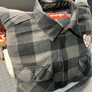 May include: A gray and black plaid flannel shirt pillow with a red "Wrangler" label and a heart-shaped patch with a message.