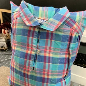 May include: A blue, pink, and green plaid pillow with a button closure. The pillow is made from a repurposed shirt with the text "Top This" on the collar.