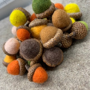 May include: A pile of felt acorns in various colours, including brown, green, orange, yellow, and pink. The acorns are all hand-crafted and have a realistic appearance.