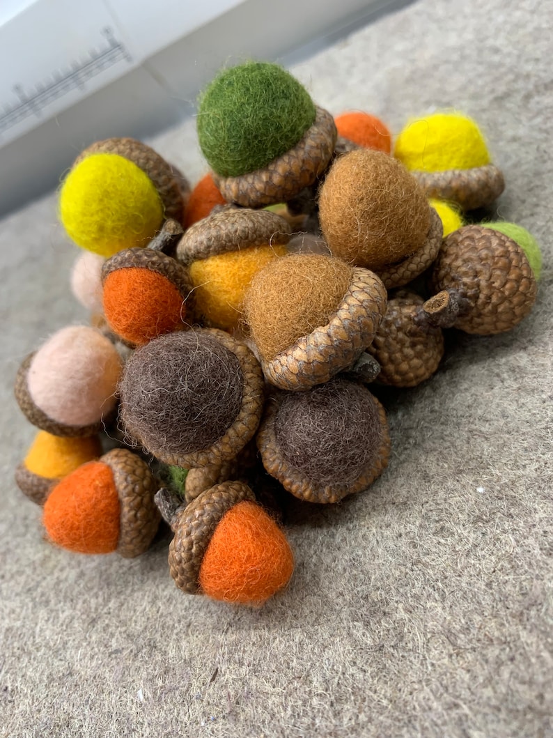 May include: A pile of felt acorns in various colours, including brown, green, orange, yellow, and pink. The acorns are all hand-crafted and have a realistic appearance.
