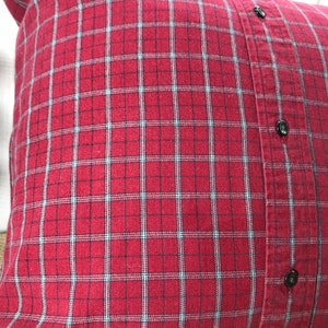 May include: A square pillow with a red and black plaid pattern. The pillow is made from a repurposed button-down shirt, with black buttons visible on the side. The pillow is a decorative home accent.