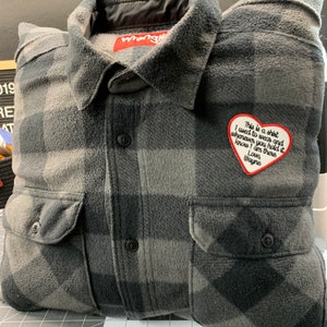 May include: A gray and black plaid flannel shirt with a heart-shaped patch that says "This is a shirt I used to wear and whenever you hold it know I am there Love Wayne".
