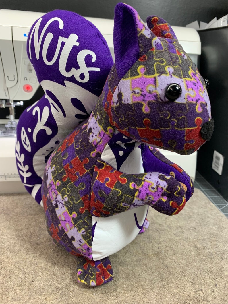 May include: Purple and white plush squirrel toy with a jigsaw puzzle pattern and the word "Nuts" on the back.