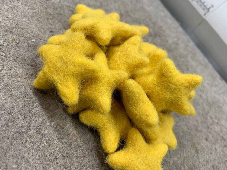 May include: A collection of yellow felt star-shaped decorations. The stars are soft and fluffy, ideal for adding a touch of whimsy to any room.