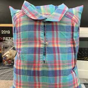 May include: A blue, pink, and green plaid pillow with a button closure and a tag that says "So This" in blue lettering.