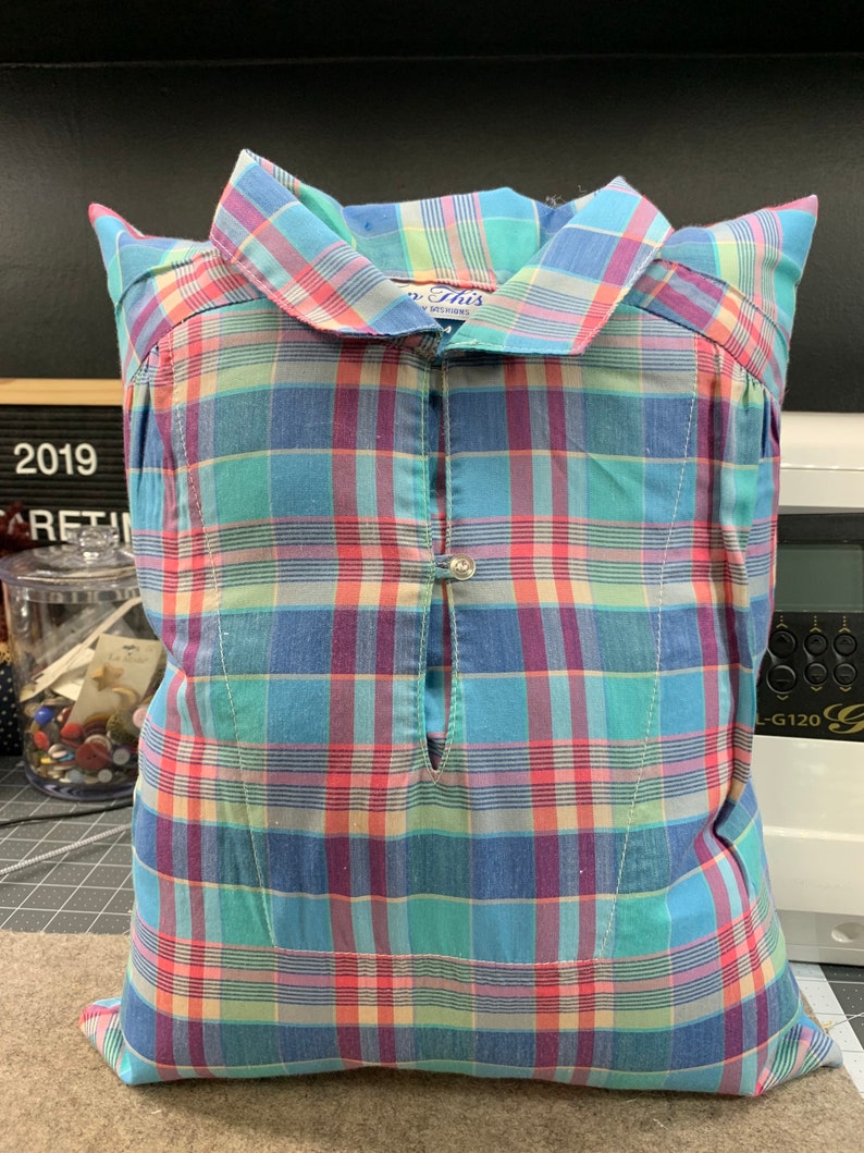 May include: A blue, pink, and green plaid pillow with a button closure and a tag that says "So This" in blue lettering.