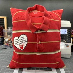 May include: Red and white striped pillow with a heart-shaped embroidered patch that says "This is a shirt I used to wear. Hold it close and I'll always be there. Dad".