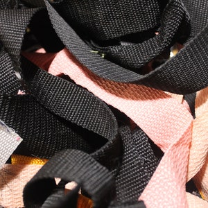 May include: A close-up of a pile of black, pink, and white webbing. The webbing is woven and has a textured surface.
