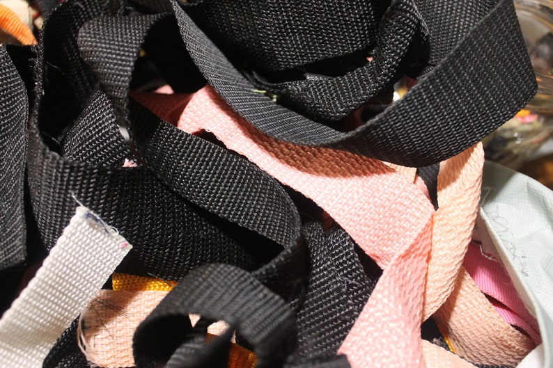 May include: A close-up of a pile of black, pink, and white webbing. The webbing is woven and has a textured surface.