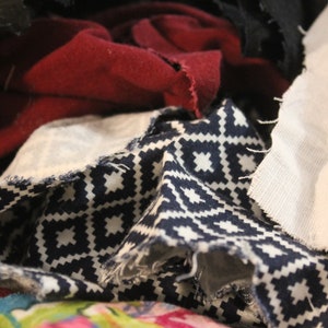 May include: A pile of fabric scraps in various colors and patterns, including black, red, white, and blue. The fabric scraps are arranged in a random order, creating a textured and colorful composition.