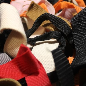May include: A close-up of a variety of woven and braided straps in different colors, including black, white, brown, red, orange, and pink.