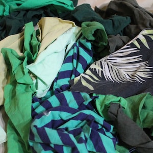May include: A pile of fabric scraps in various shades of green, blue, and beige. The fabric scraps are made of cotton and have different patterns, including stripes and a tropical leaf design.