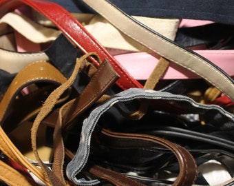 May include: A close-up of a pile of different colored leather straps, including brown, tan, black, red, and pink. The straps are woven together and appear to be part of a bag or purse.