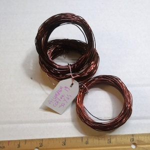 May include: Two spools of copper wire, one larger than the other. The larger spool has a white tag attached with the text "Aluminum Coffee 19 38 Yrs".