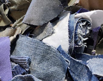 May include: A close-up shot of a pile of denim fabric scraps in various shades of blue, white, and gray. The pieces are torn and frayed, with visible stitching and textures. Some pieces are a solid color, while others have a classic denim weave.