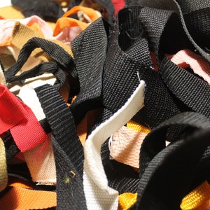 May include: A pile of colorful fabric ribbon scraps in various widths and textures, including black, white, red, orange, pink, and brown.