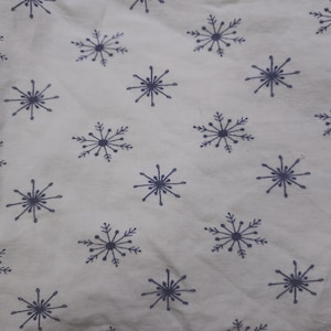May include: A white fabric featuring a repeating pattern of dark blue, hand-drawn style snowflake illustrations. Each snowflake consists of a central dot with radiating lines ending in small dots, creating a simple, consistent winter-themed design.