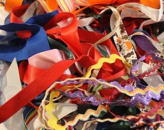 May include: A pile of colorful ribbons and trims in various textures and patterns, including red, blue, yellow, purple, and white.