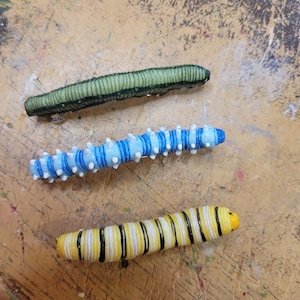 K&ouml;nnte beinhalten: Drei Plastikraupen, eine gr&uuml;ne, eine blaue mit wei&szlig;en Streifen und eine gelbe mit schwarzen Streifen.