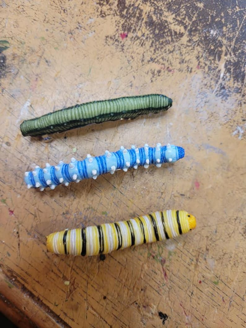 K&ouml;nnte beinhalten: Drei Plastikraupen, eine gr&uuml;ne, eine blaue mit wei&szlig;en Streifen und eine gelbe mit schwarzen Streifen.