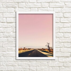 May include: A framed photograph of a desert road stretching into the distance under a pink sky. A lone, dead tree stands on the right side of the road.