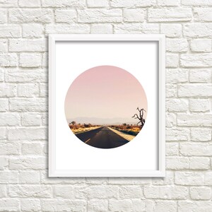 Puede incluir: Una impresi&oacute;n enmarcada de una fotograf&iacute;a circular que muestra un camino del desierto que conduce a la distancia bajo un cielo rosado.