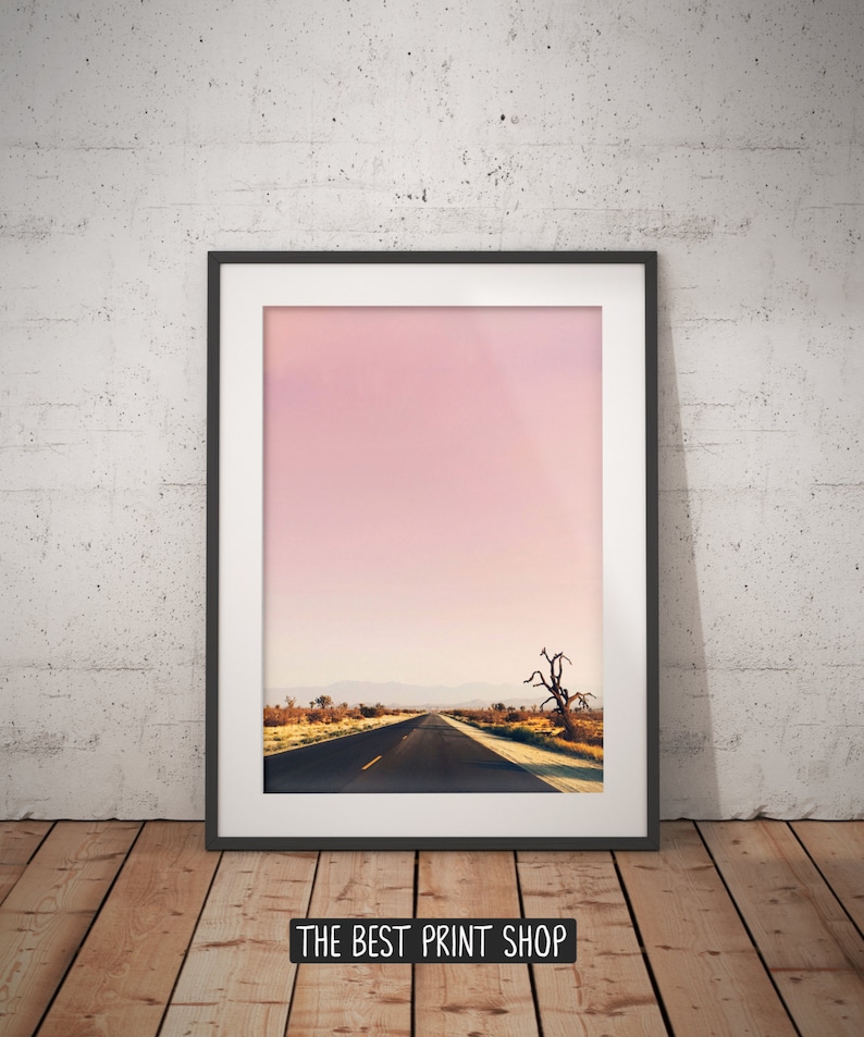May include: A framed photograph of a long, straight road leading into the distance. The road is surrounded by desert landscape with a single, dead tree in the foreground. The sky is a soft pink color.