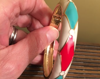 May include: A gold bangle bracelet with a white, red, and turquoise enamel design. The bracelet has a hinged clasp.