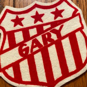 May include: A white felt patch with red stripes and three red stars. The word "GARY" is written in red felt across the patch.