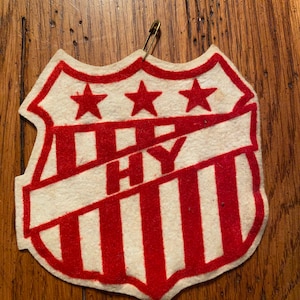 May include: A red, white, and blue felt patch with three stars and the letters "HY" in the center. The patch is shaped like a shield and has a safety pin attached.