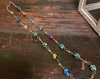 May include: A gold chain necklace with colorful glass beads. The beads are oval shaped and have a black background with multi-colored designs.