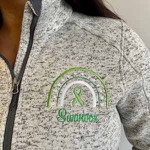 May include: A gray heather zip-up jacket with a green embroidered rainbow and ribbon, and the word "Survivor" underneath.