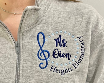 May include: Gray zippered sweatshirt with a blue embroidered design featuring a treble clef, the text "Ms. Dien", and "Heights Elementary" in a circle.
