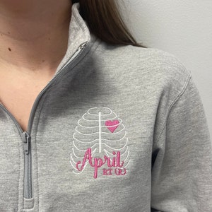 May include: Gray sweatshirt with a white embroidered ribcage design and a pink heart. The text "April RT (R)" is also embroidered in white.