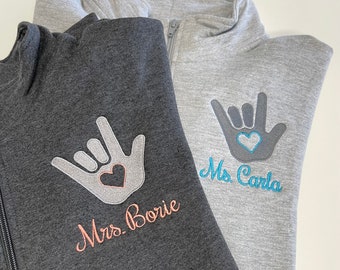 May include: Two gray sweatshirts with a hand sign and the text "Mrs. Borie" and "Ms. Carla" embroidered on them.