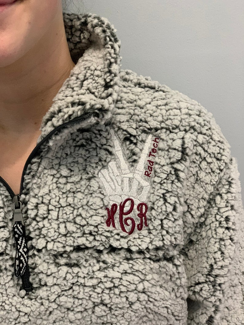 May include: A gray sherpa pullover with a maroon monogram and the text "Rad Tech" embroidered on the right shoulder.